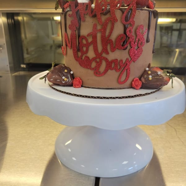 Chocolate Mother's Day cake with red glitter lettering, chocolate drizzle, and strawberries on a white stand.