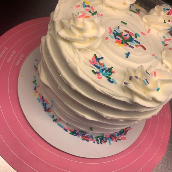 Sweet Antojito's white frosted cake with colorful sprinkles and decorative icing swirls.