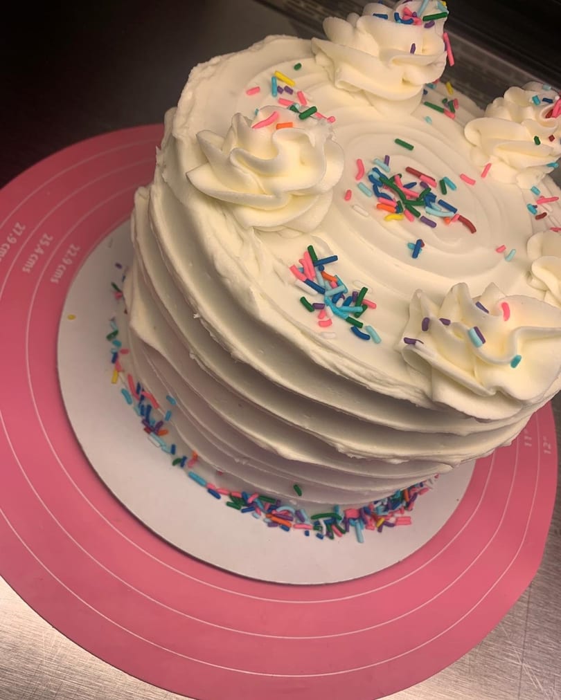 Sweet Antojito's white frosted cake with colorful sprinkles and decorative icing swirls.